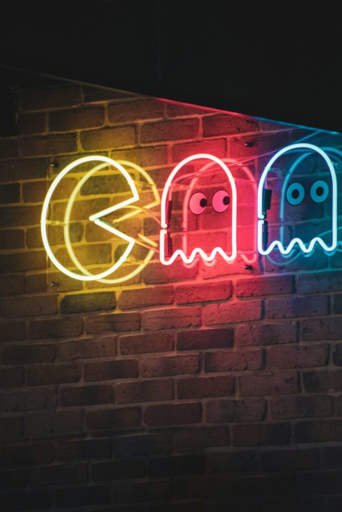 Neon Pac-Man with neon ghosts Pinky and Inky mounted on a brick wall.