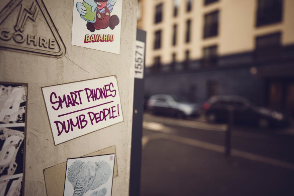 sticker reading “Smart Phones | Dumb People!” on an electrical cabinet in the foreground of a street scene