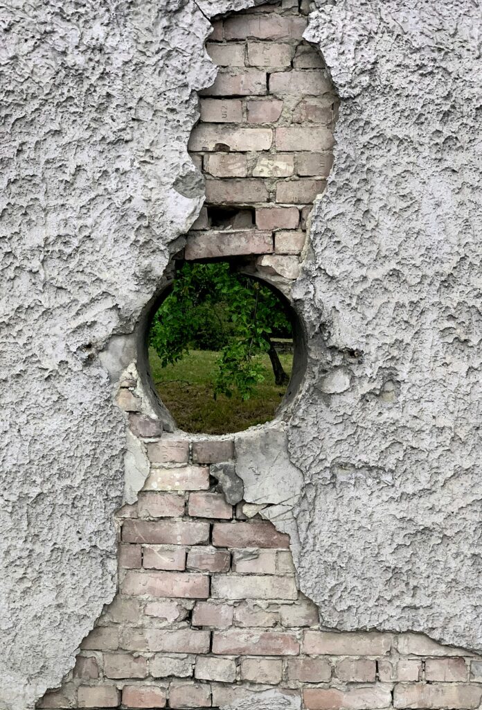 concrete and brick wall with circular hole, with grass and a tree visible though it