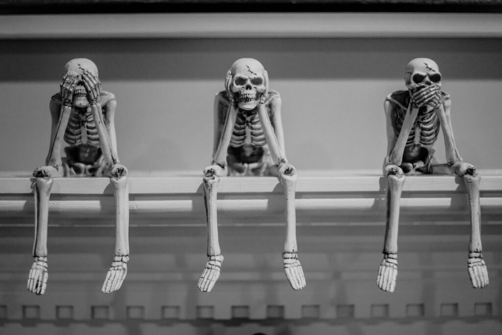 Spooky skeletons sitting on a mantle that see no evil, hear no evil and say no evil